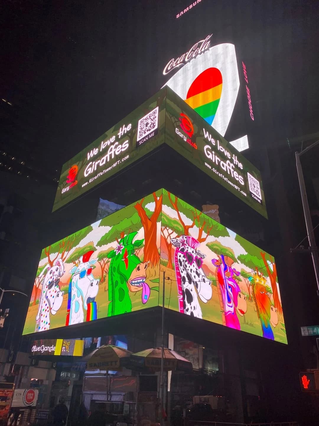 Giraffe Tower artwork and a Gary Club billboard reading ‘We love the Giraffes’ lighting up Times Square at night